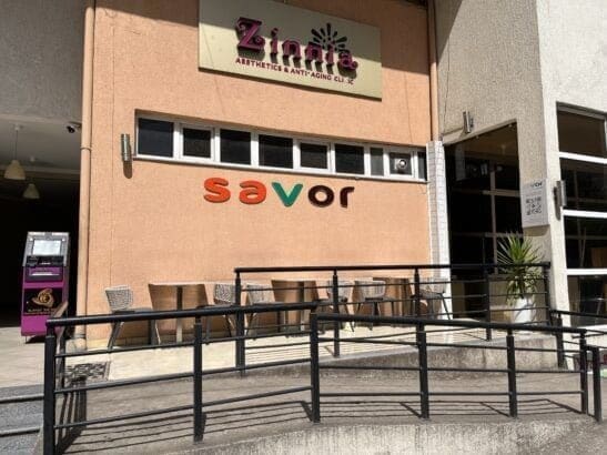 Exterior view of Savor restaurant with outdoor seating and a beige wall with the "savor" sign.
