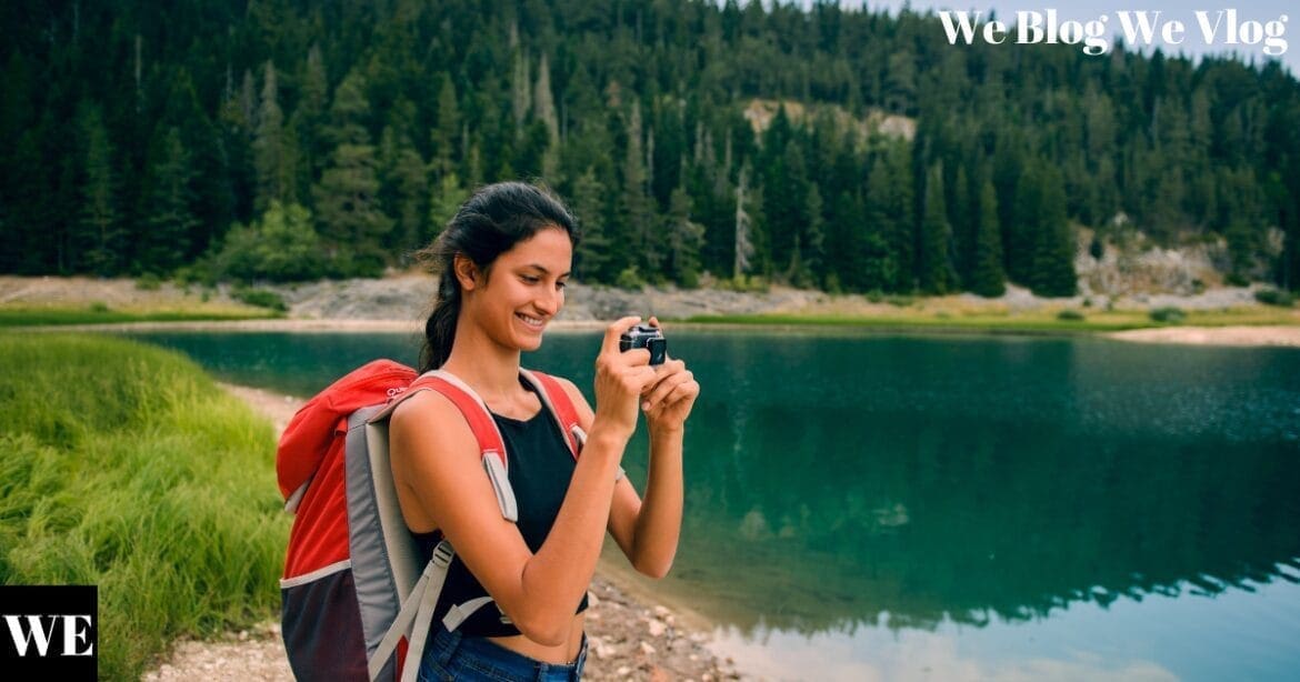 A woman in casual attire photographing a scenic nature landscape, surrounded by lush greenery and vibrant light.