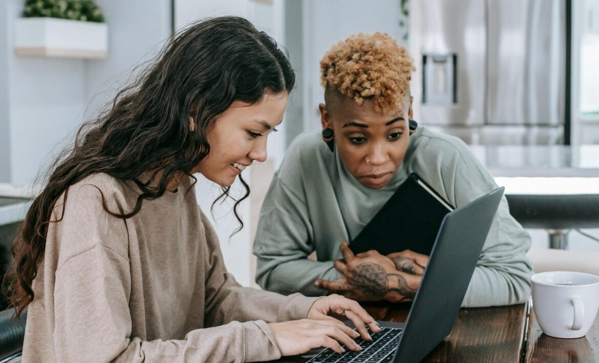 Two young women laughing while looking at a computer screen, representing enjoyment and engagement with humorous content