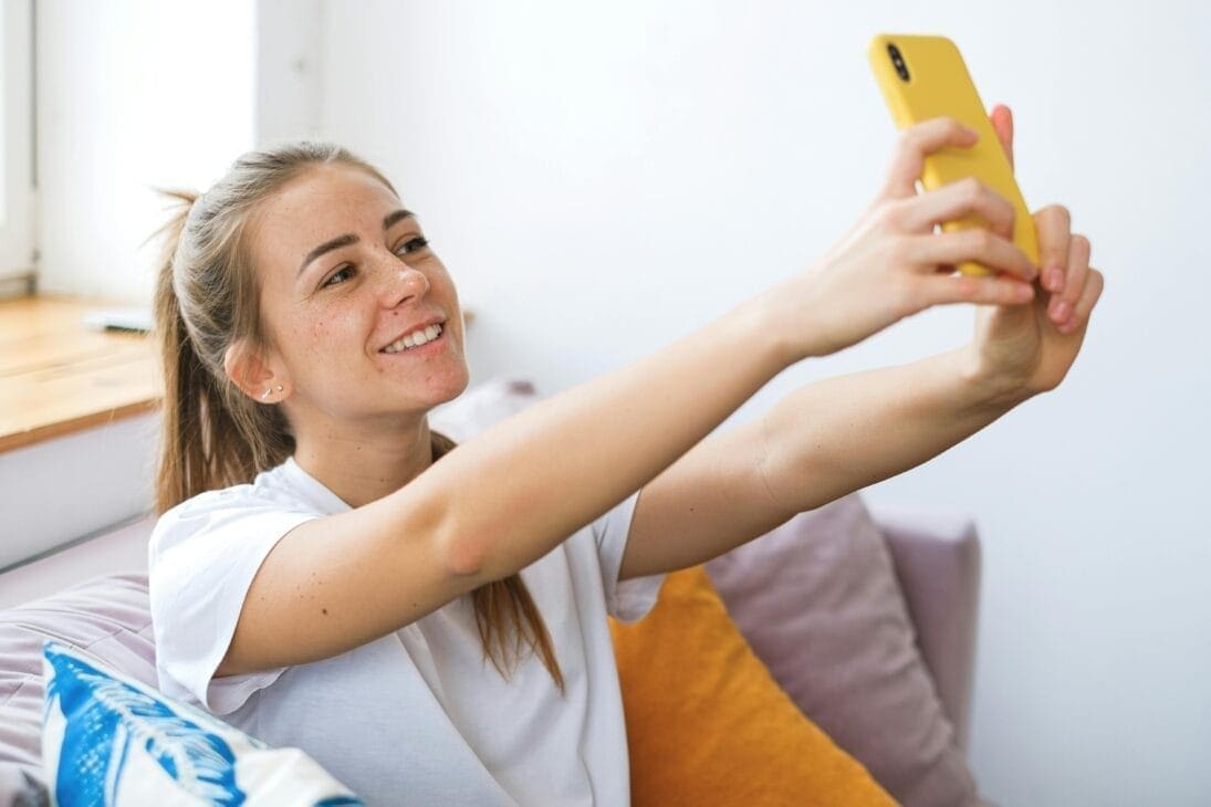 Young woman smiling happily while taking a selfie on her smartphone.
