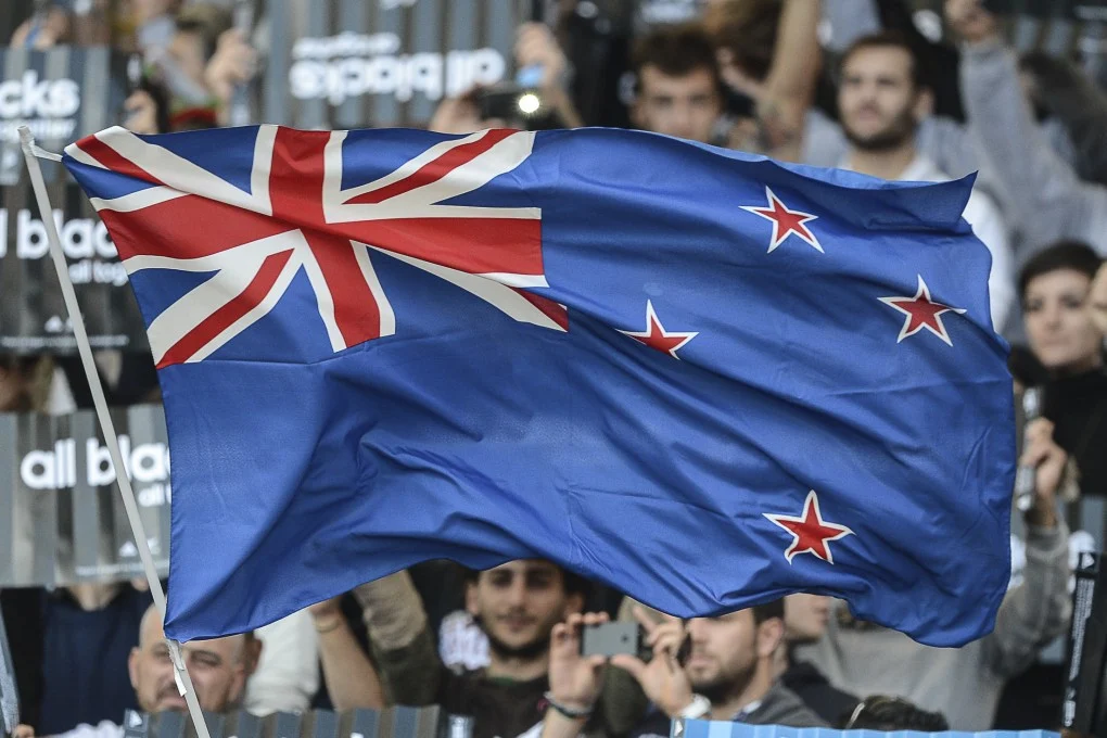 Group of New Zealanders proudly holding the New Zealand culture flag at a public event, symbolizing national unity and Kiwi identity.