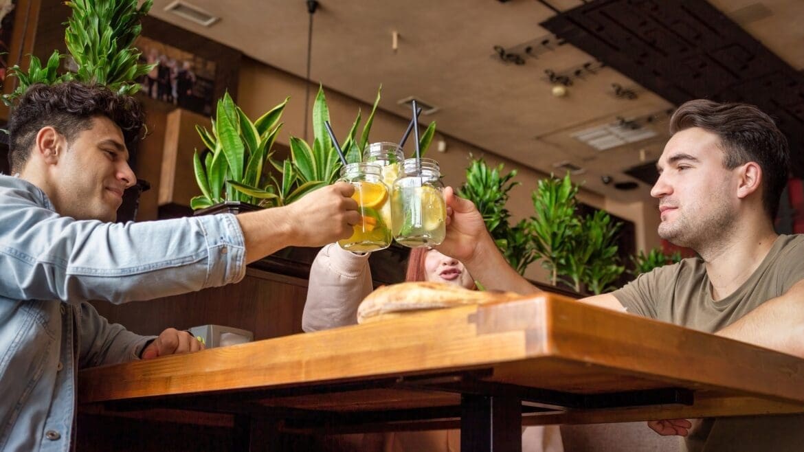 Two friends clinking glasses of non-alcoholic drinks in a cozy café setting.