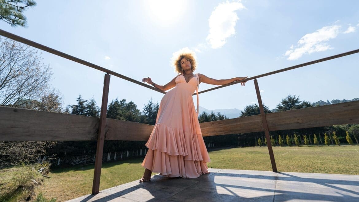 Woman posing outdoors in a long flowing dress, angled slightly with natural lighting highlighting her features.