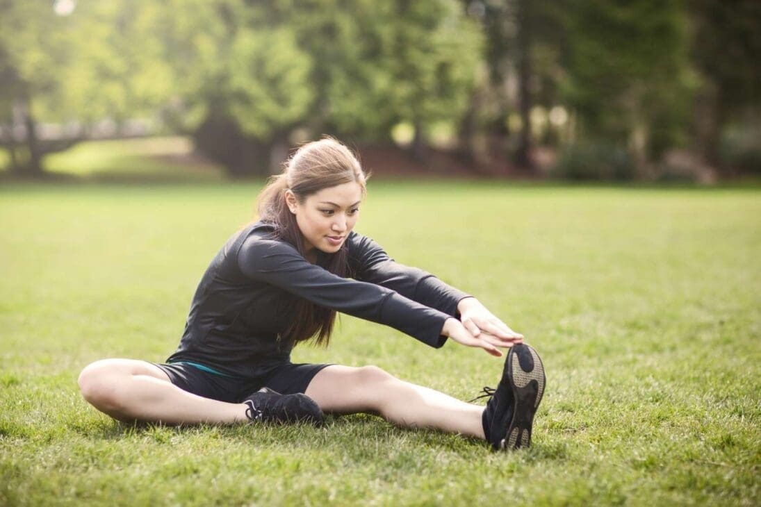 Woman performing quick standing stretches, including a calf stretch at a bench, demonstrating easy 2–3 minute mobility exercises during a walk.