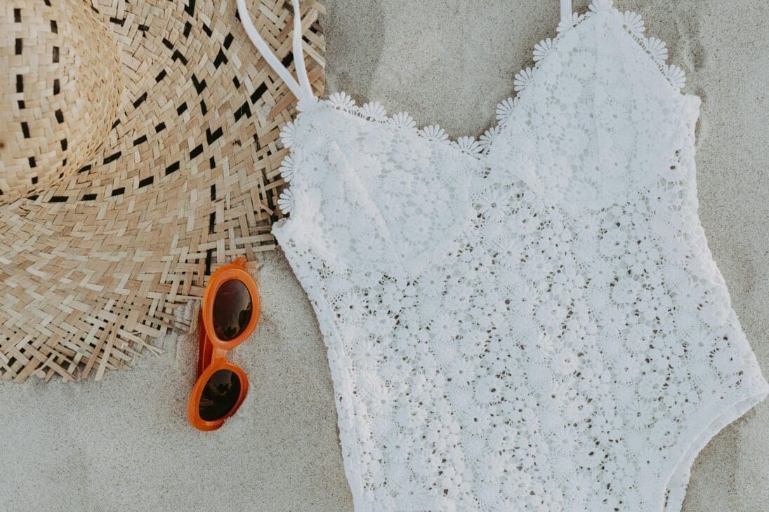Flat lay of summer swimwear guide featuring textured fabrics, bold prints, and neutral with accessories like sunglasses, a straw hat, and sandals.